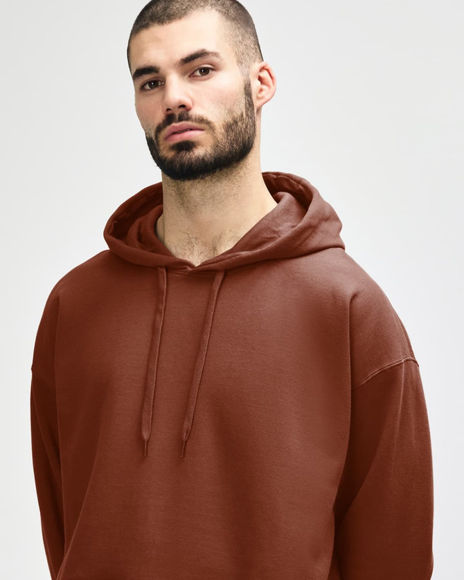 A woman wearing a brown Gildan Softstyle adult hooded sweatshirt, holding the hood with both hands.