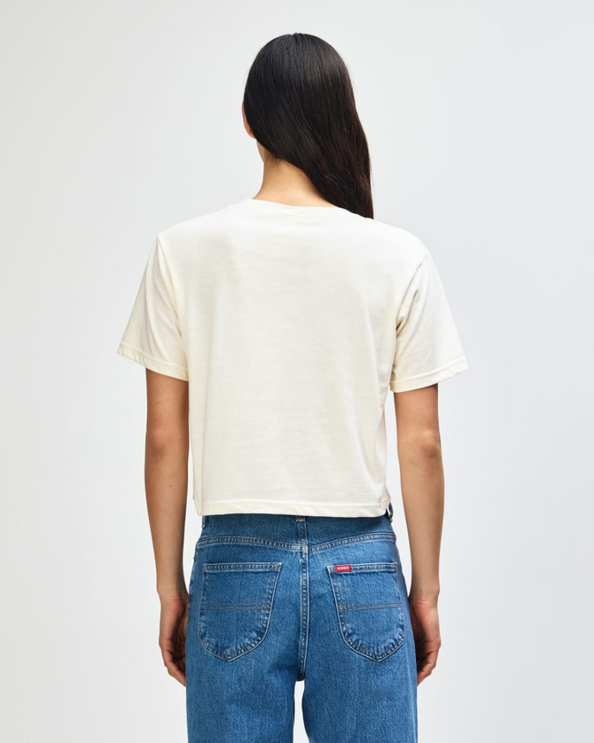 A beige women's boxy t-shirt with short sleeves, viewed from the back, featuring a logo. Casual style, perfect for layering.