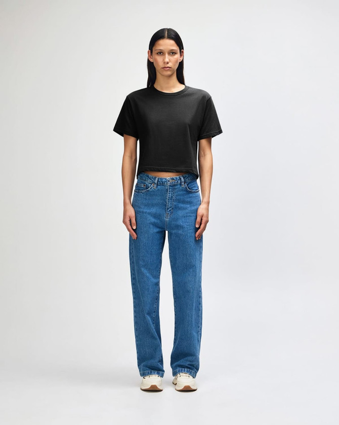 A woman wearing a black boxy T-shirt and wide-leg blue jeans, standing against a white background.