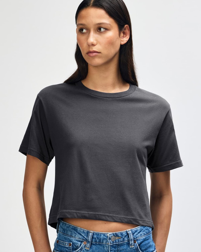 A woman models a grey boxy T-shirt with short sleeves and a relaxed fit, paired with light denim jeans.