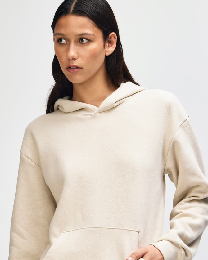 A unisex hooded sweatshirt in a light cream colour, featuring a front pocket and a logo.