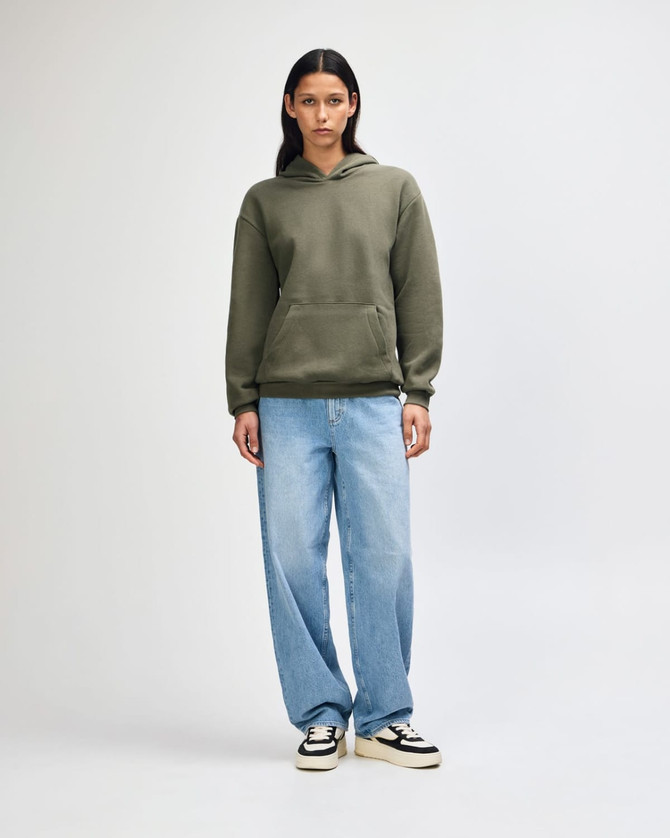 A model wearing an olive green unisex hooded sweatshirt, paired with black cargo pants and sneakers.