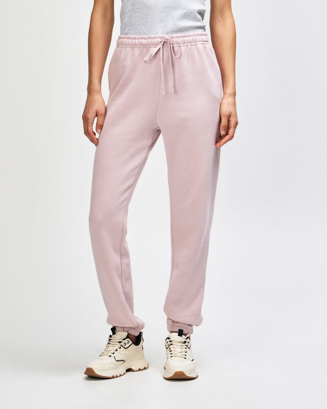 Unisex sweatpants in soft pink, featuring an elastic waistband and cuffs, shown with a pair of sneakers.