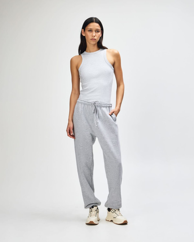 Unisex sweatpants in grey, featured with a cropped cream top, model standing in casual pose, includes branding.
