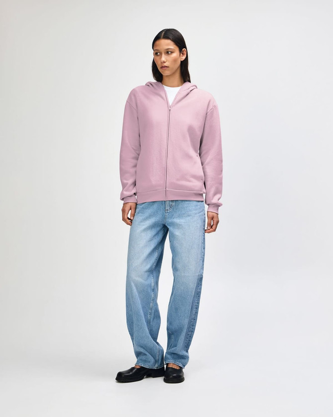 A unisex full zip hooded sweatshirt in soft pink, featuring a relaxed fit and a front zip. It has a logo.