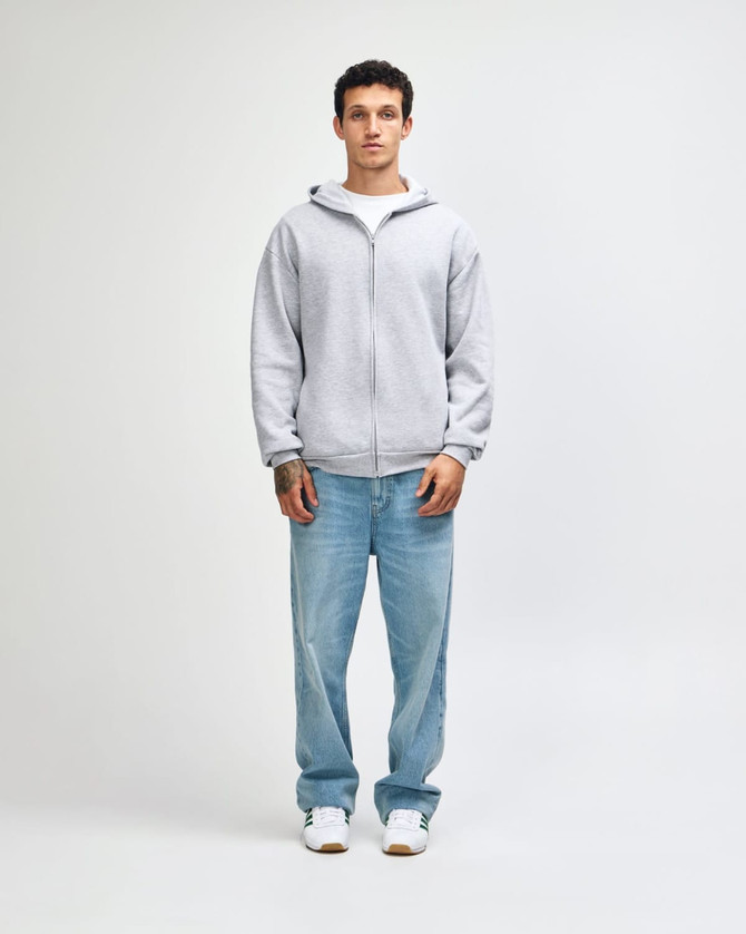 A unisex full zip hooded sweatshirt in grey, worn with blue jeans and white sneakers, featuring a logo.