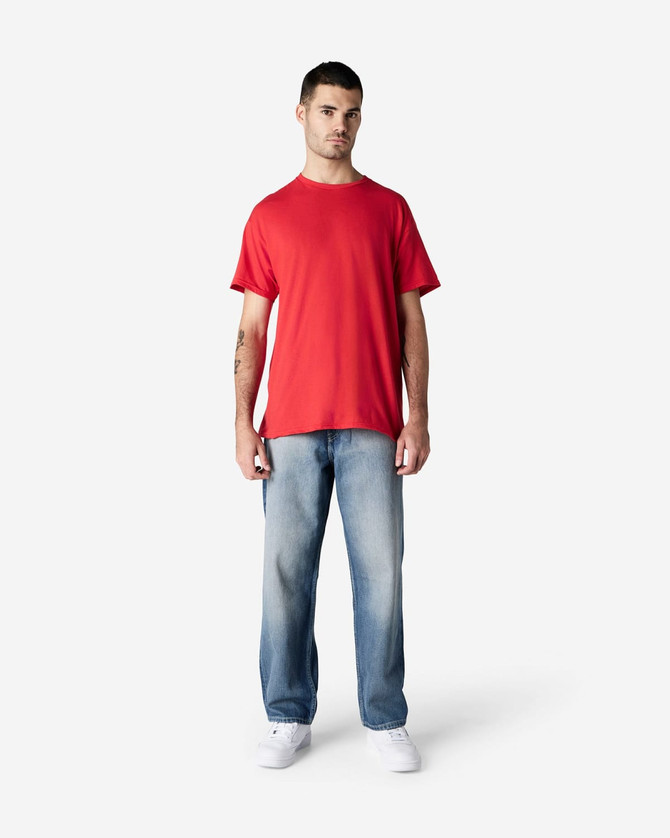 A red Gildan Light Cotton T-Shirt displayed on a standing model, paired with light blue jeans. The model has a casual pose.