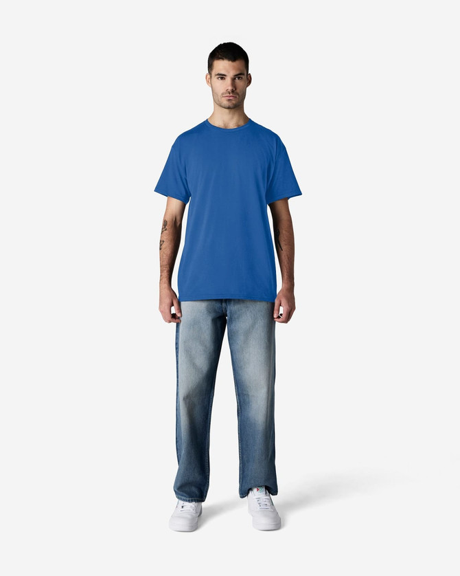 A blue Gildan Light Cotton T-Shirt displayed on a model, paired with light denim jeans and white shoes, featuring a logo.
