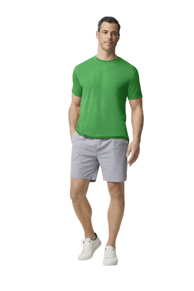 A man wearing a green Gildan Performance adult t-shirt and grey shorts, standing casually. The shirt features a logo.