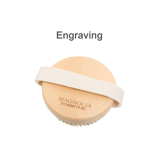 A round exfoliating brush with soft massage nodules, featuring a wooden top and a fabric strap. Includes branding.