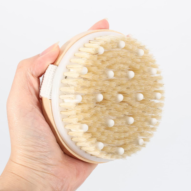 An exfoliating brush featuring soft massage nodules and natural bristles, held in a hand. The brush has a wooden base.