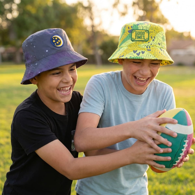 Two children wearing custom bucket hats, one in purple with a logo and the other in yellow with a patch, laughing while holding a football.