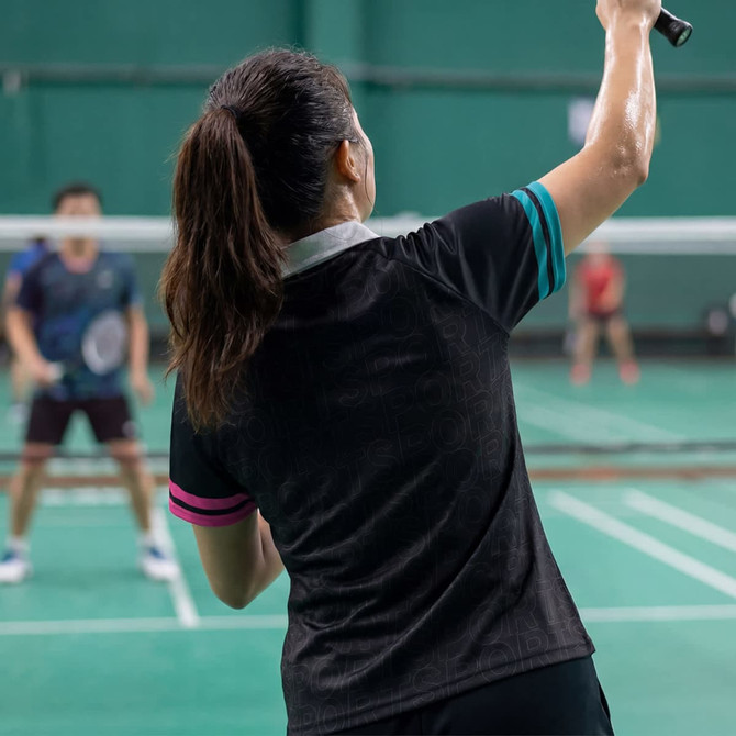 A women's active polo shirt in black with turquoise and pink accents, featuring a logo.
