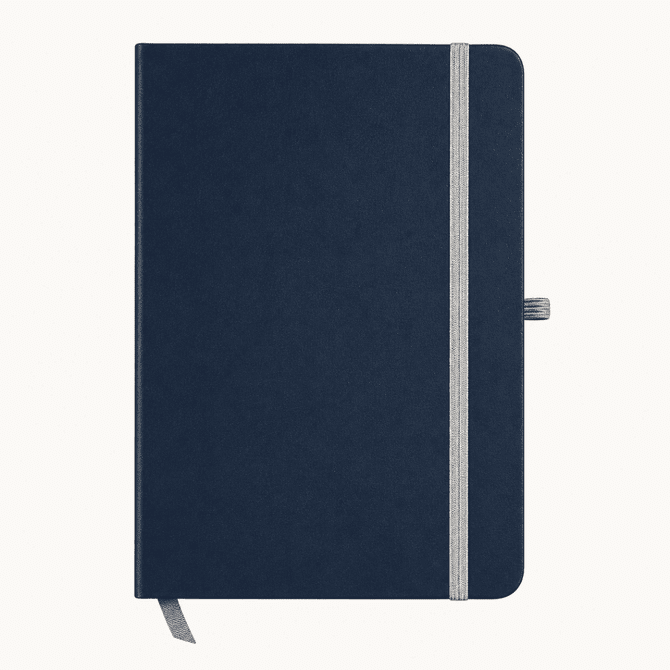 A navy blue A5 notebook with a grey elastic band and a ribbon bookmark. It features a logo on the cover.