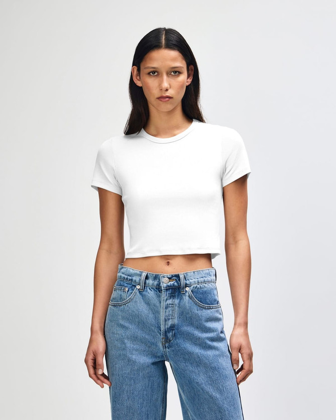 A white women's crop fitted T-shirt paired with blue high-waisted jeans, featuring a simple design and a logo.