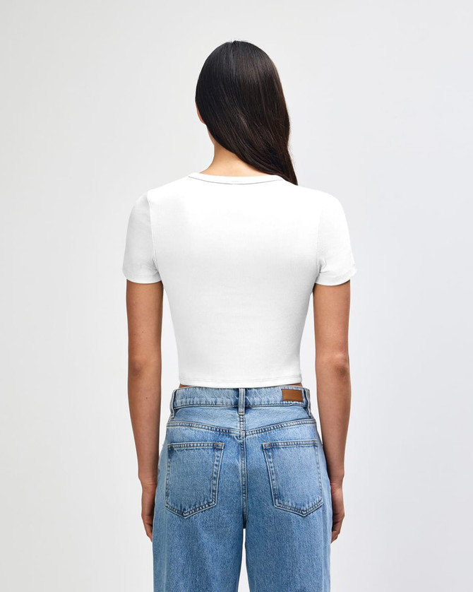 A white women's crop fitted t-shirt with a short sleeve design, displayed from the back, paired with blue jeans.
