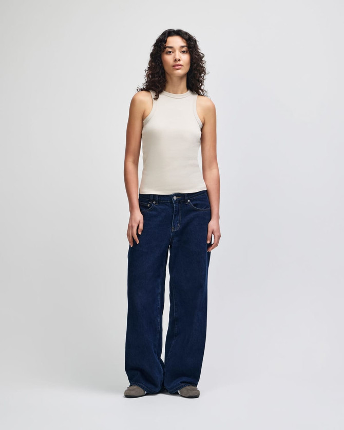 A fitted tank in beige worn with wide-leg denim jeans, featuring a model against a plain background.
