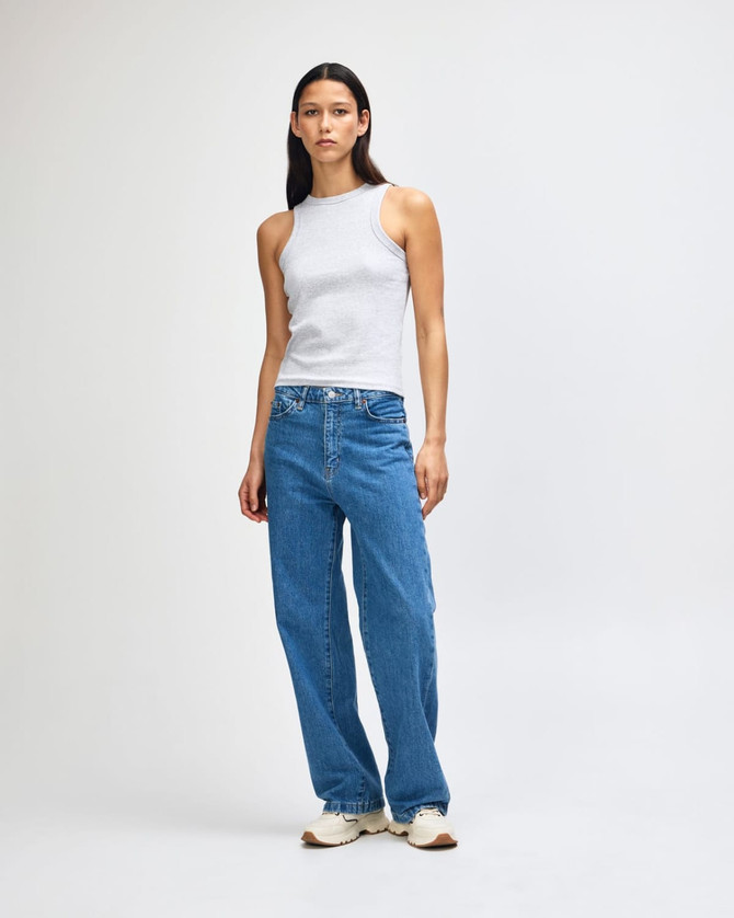 A fitted tank top in light grey, paired with blue jeans. The model stands against a plain background.