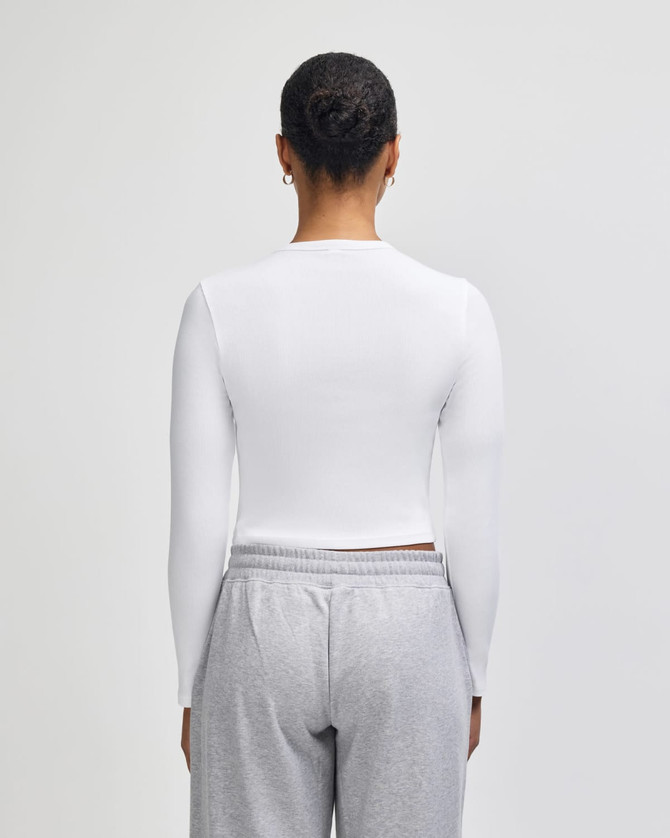 A white long-sleeve cropped fitted t-shirt viewed from the back, paired with grey pants.