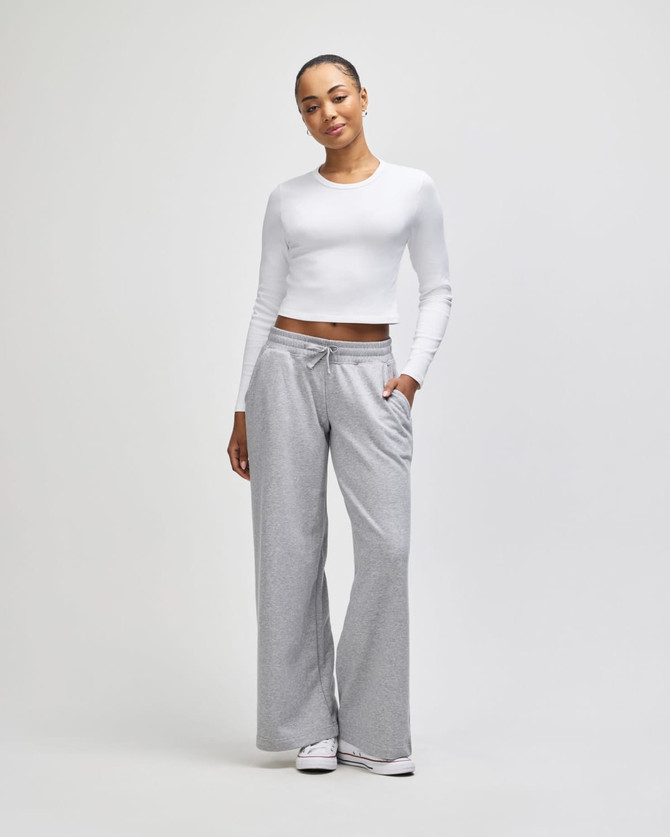A fitted white long-sleeve crop top paired with grey wide-leg trousers, featuring pockets and a relaxed fit.