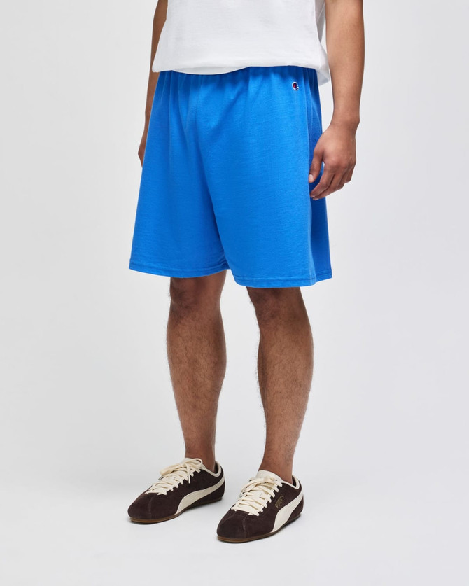 Bright blue cotton gym shorts with an elastic waistband and a logo, worn by a person standing.