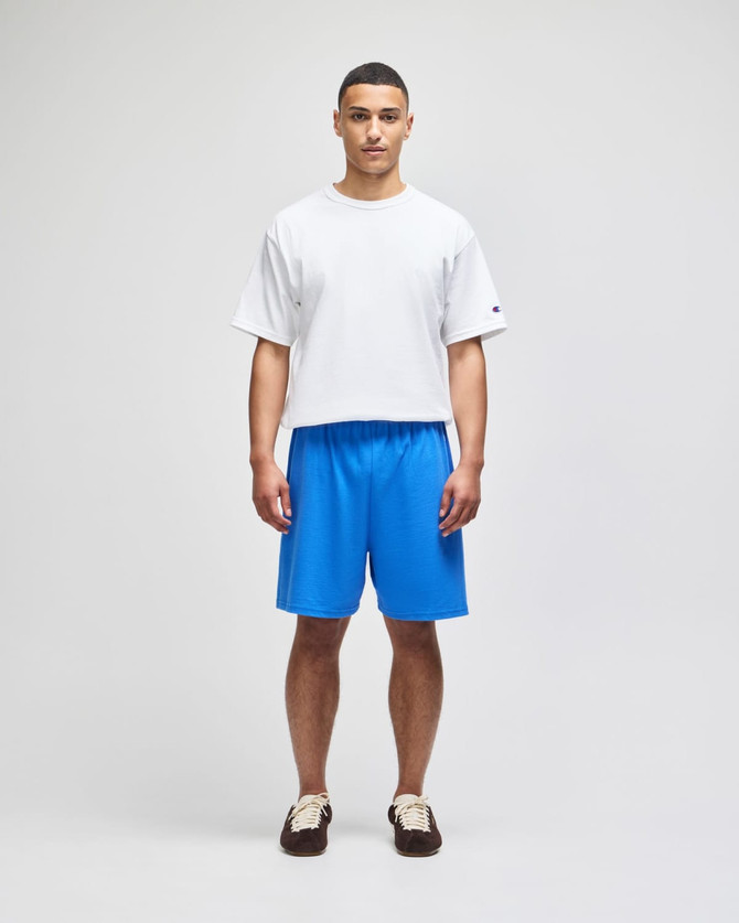 A model stands wearing blue cotton gym shorts and a white t-shirt, featuring a logo on the shirt.