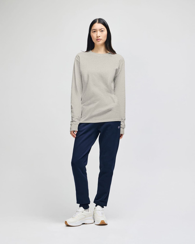 A long-sleeve t-shirt in a light grey colour, worn with navy pants, featuring a logo on the shirt.