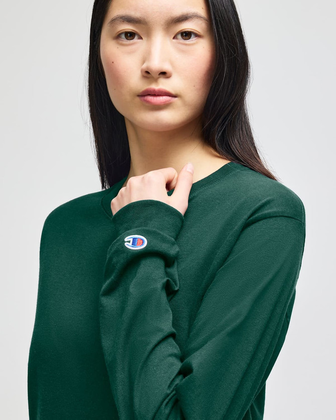 An olive green long-sleeve t-shirt featuring a small logo on the sleeve, modelled by a woman.