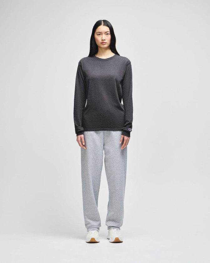 A model wearing a grey Champion long-sleeve T-shirt paired with grey sweatpants and sneakers. The shirt has a logo.
