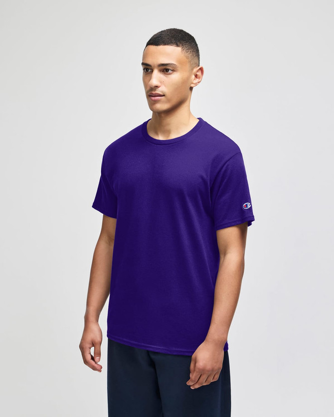 A purple Champion adult jersey short sleeve T-shirt displayed on a male model, featuring a logo on the sleeve.