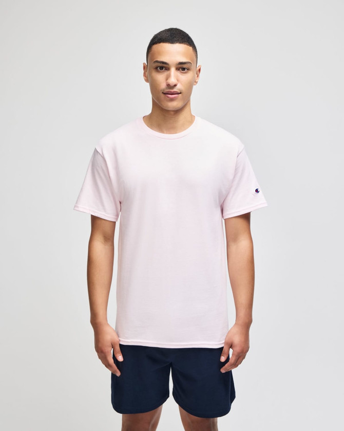 A light pink short sleeve jersey T-shirt with a logo on the sleeve, worn by a model standing against a plain backdrop.