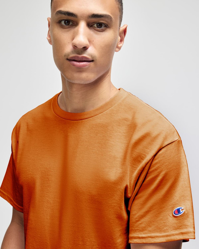 An adult jersey short sleeve t-shirt in orange, featuring a logo on one sleeve.