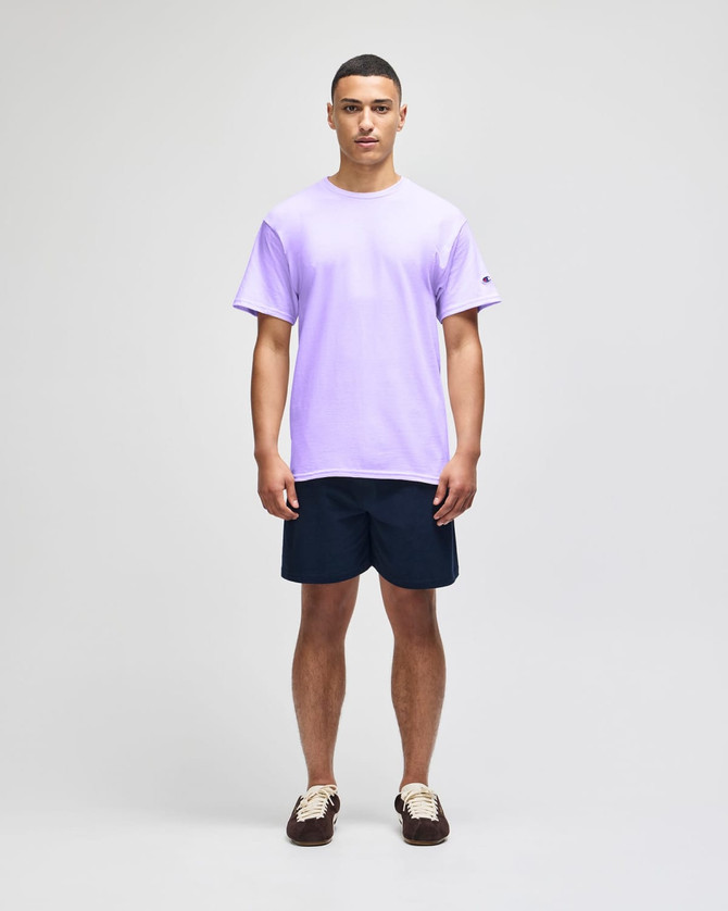 A purple short sleeve t-shirt on a model, paired with navy shorts, featuring a brand logo.