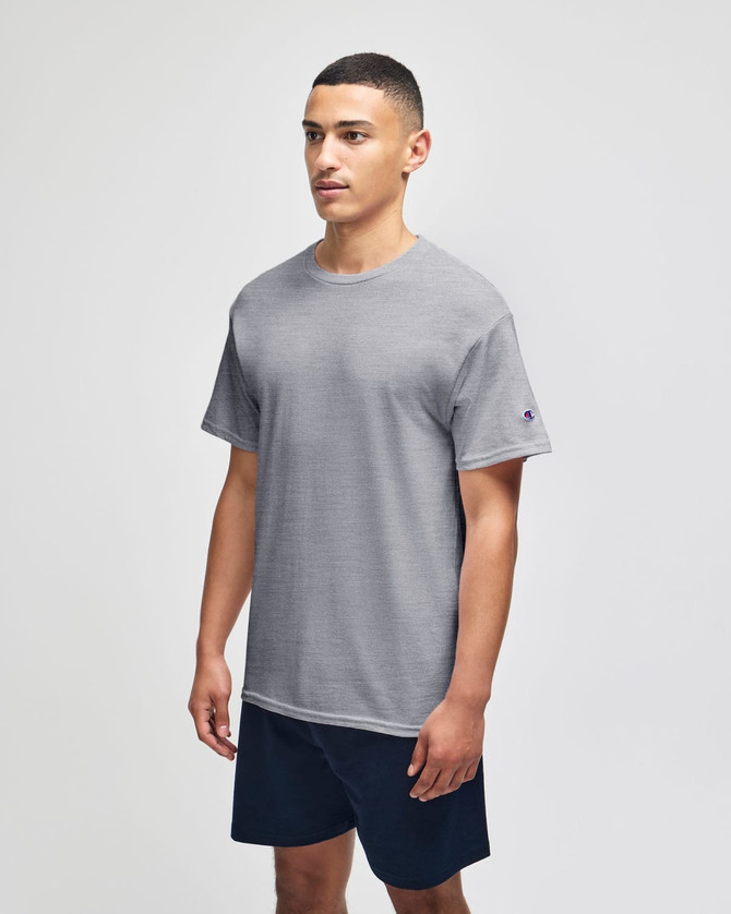 A grey short sleeve t-shirt with a logo, worn by a model, paired with navy shorts.