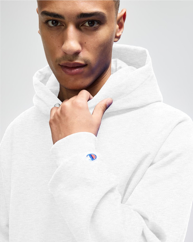 A light grey pullover hooded sweatshirt featuring a logo, worn by a young man with short hair.