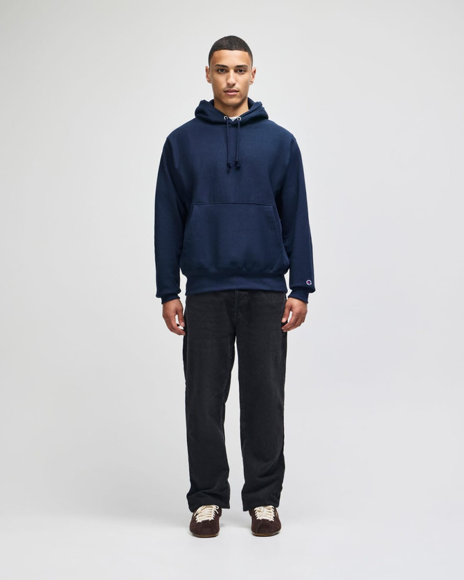 A navy blue pullover hooded sweatshirt with a front pocket and drawstring hood, paired with dark trousers.