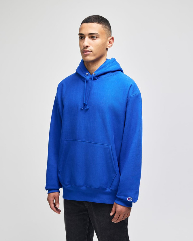 A blue pullover hooded sweatshirt features a front pocket and a logo. The model stands against a neutral background.