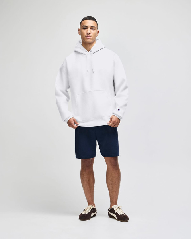 A white pullover hooded sweatshirt paired with navy shorts, featured on a model. The sweatshirt has a logo.
