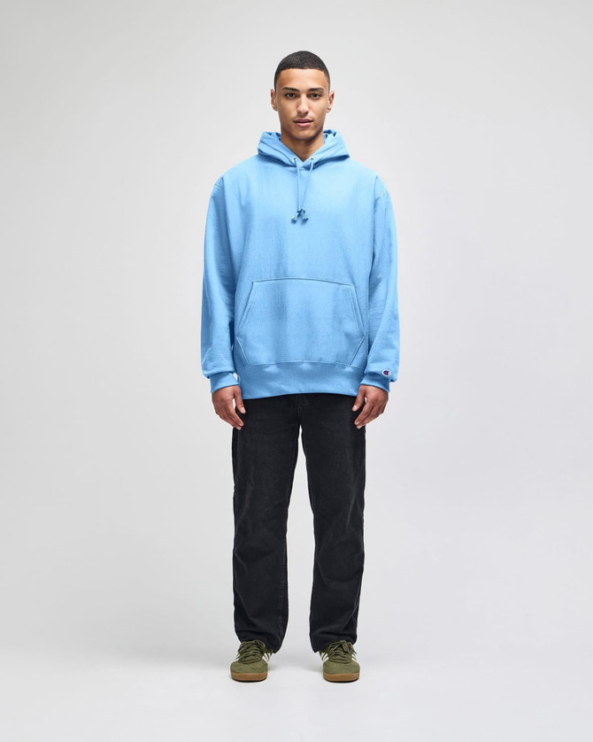 A light blue hooded sweatshirt with a front pocket, worn by a model standing against a neutral background.