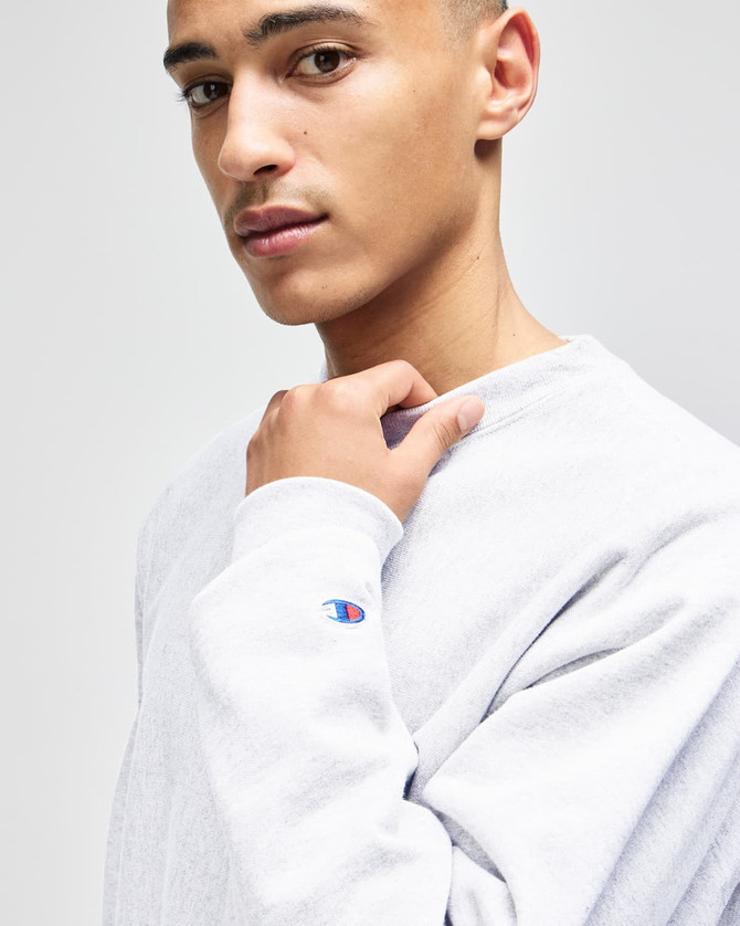 A grey Champion Reverse Weave® adult crew sweatshirt with a logo on the sleeve, modelled by a young man.