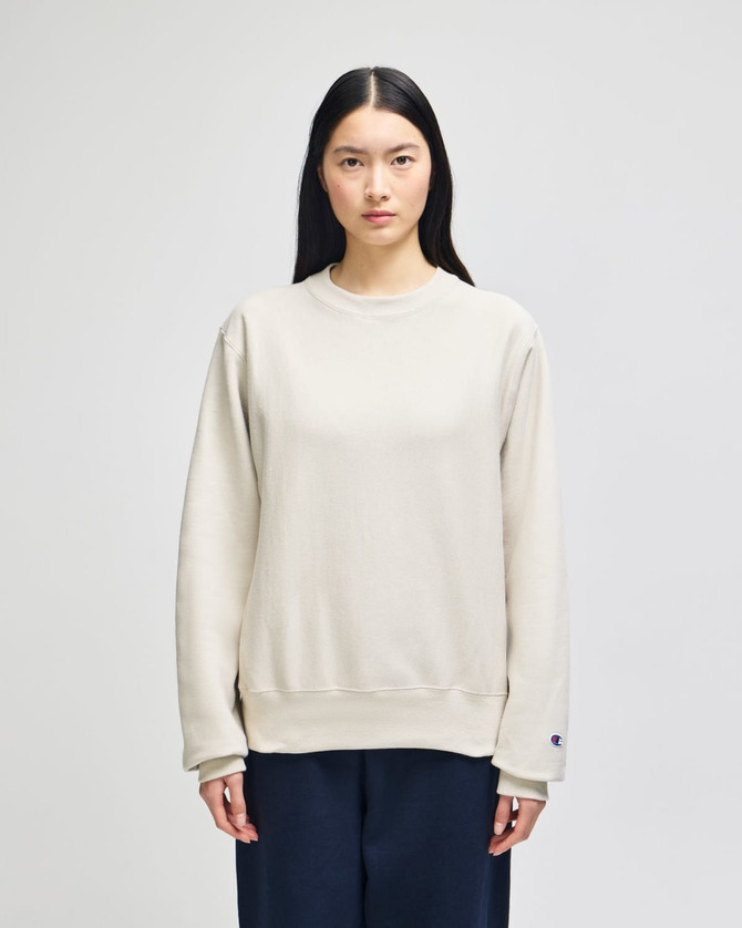 A light beige adult crew sweatshirt, featuring long sleeves and a subtle logo, displayed on a model.