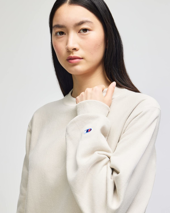 A light beige crew sweatshirt with a logo on the sleeve, featured on a model.