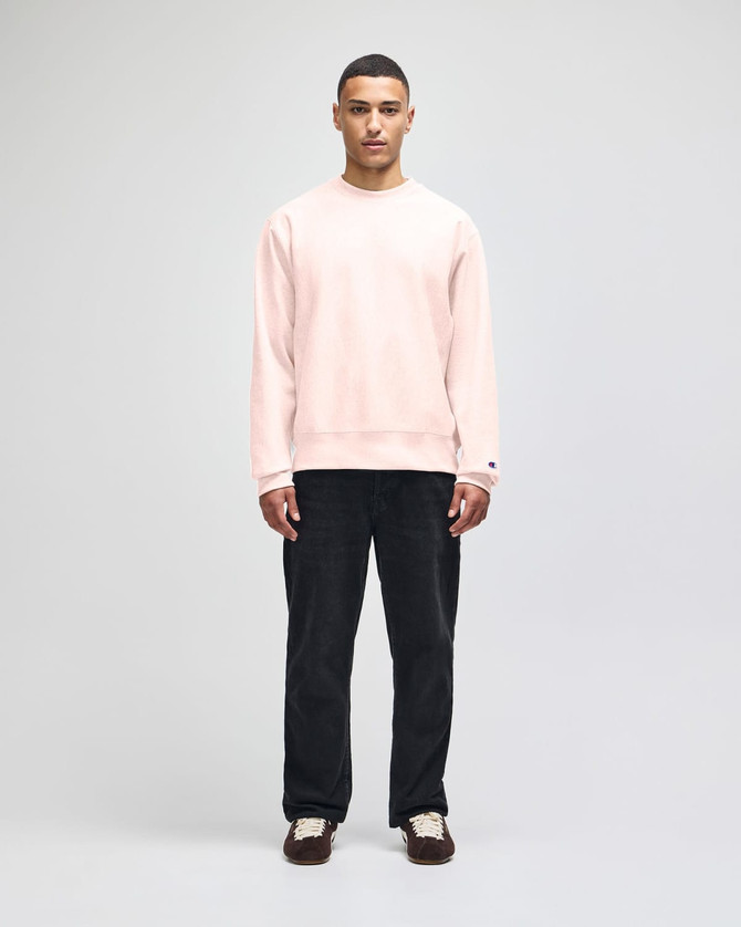 A model wearing a beige Champion Reverse Weave® adult crew sweatshirt and navy trousers, featuring a logo.