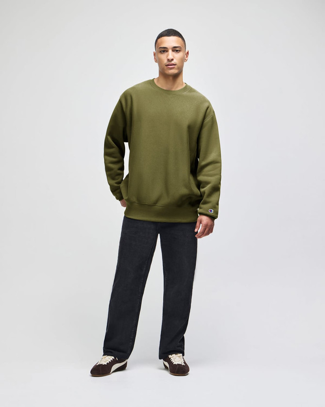 An olive green Champion Reverse Weave® adult crew sweatshirt worn by a model, paired with dark trousers.