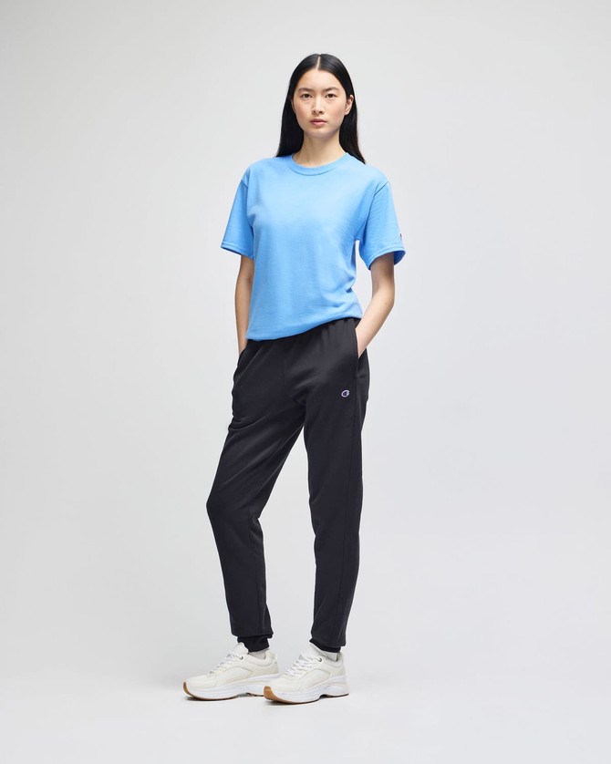 A female model wearing a blue t-shirt and black fleece joggers, featuring a logo on the joggers.