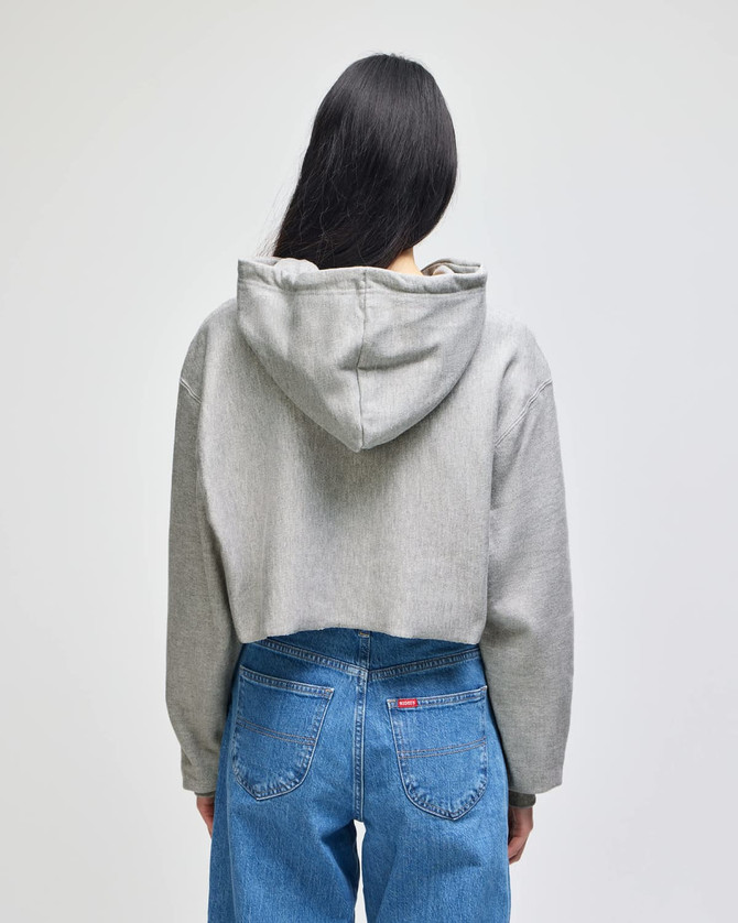 A cropped grey hoodie with a hood, viewed from the back, paired with blue jeans. It features a branding logo.