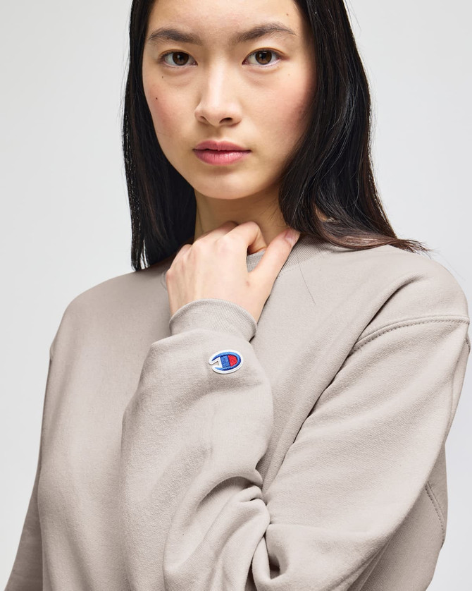 A cream-coloured crewneck sweatshirt with a logo on the sleeve, worn by a model.