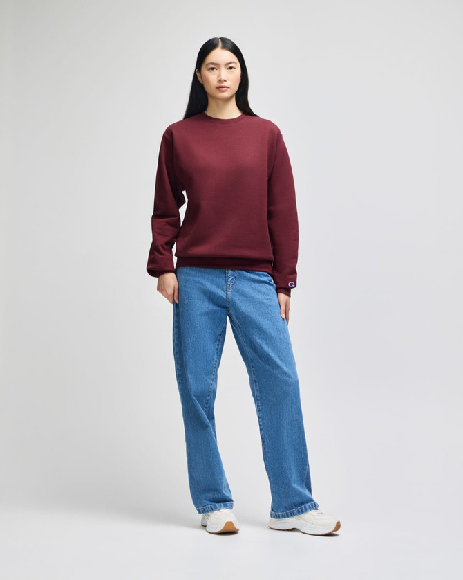 A maroon crewneck sweatshirt paired with light blue baggy jeans, worn by a female model. The sweatshirt has a logo.