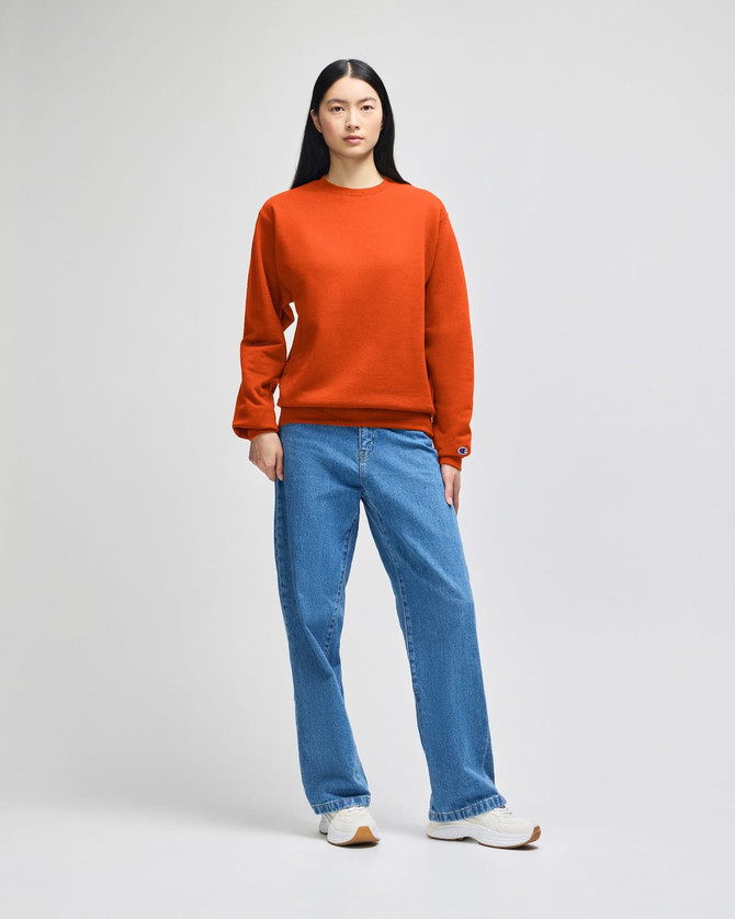 An orange crewneck sweatshirt paired with light blue jeans, worn by a model against a neutral background.
