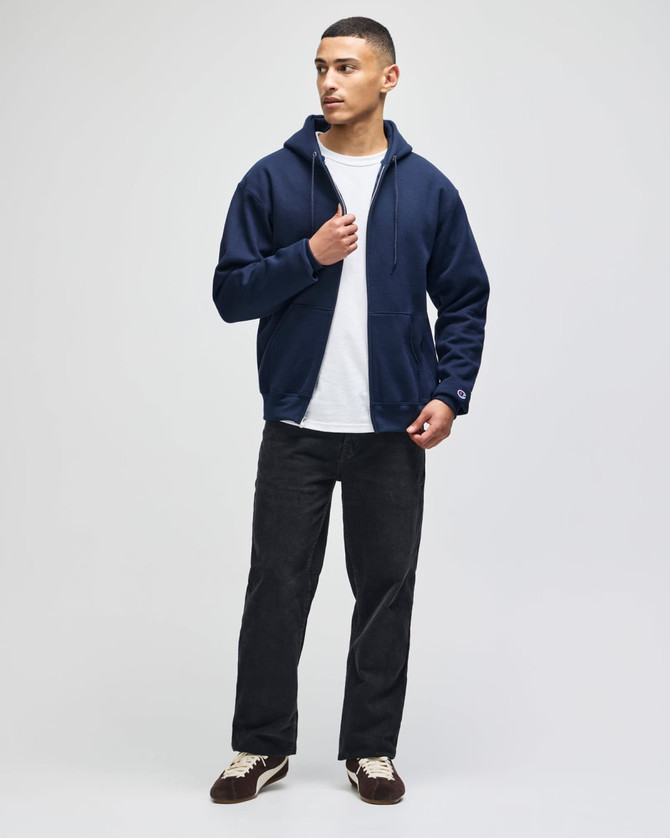 A man wearing a navy full-zip hooded sweatshirt paired with a white T-shirt and black pants.